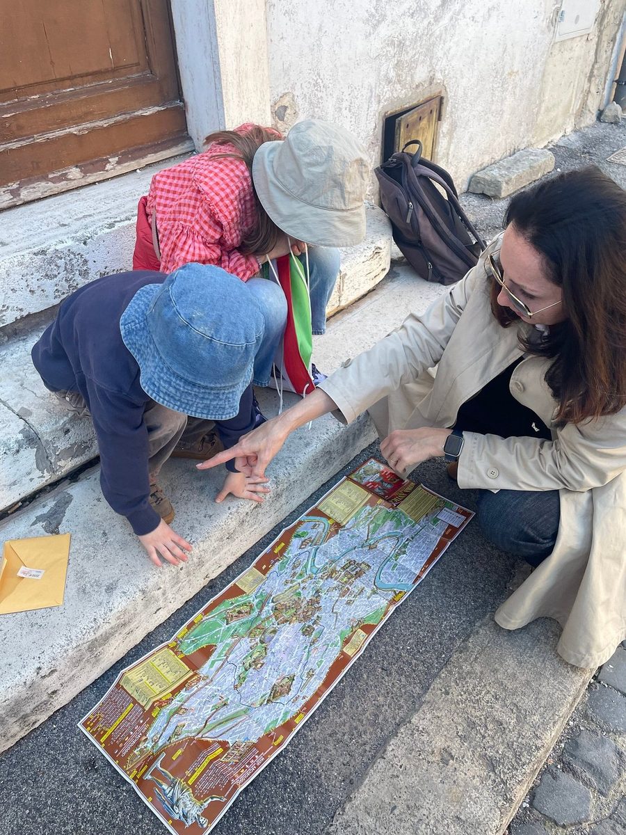 Children and the guide unroll a long scroll map on the cobblestones