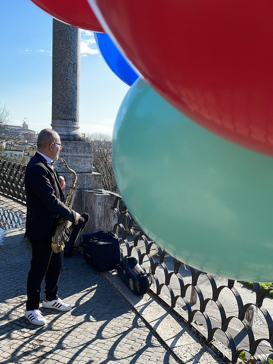 A saxophonist plays at a viewpoint, balloons nearby
