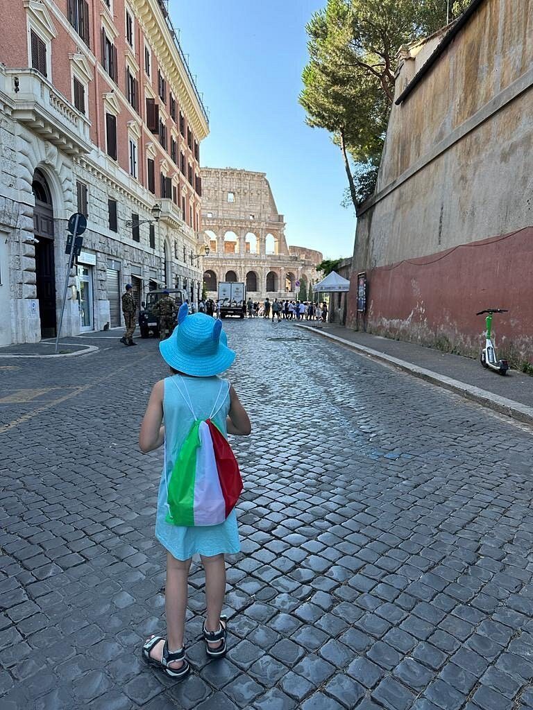 A child with an Italian flag walks along the street towards the Colosseum