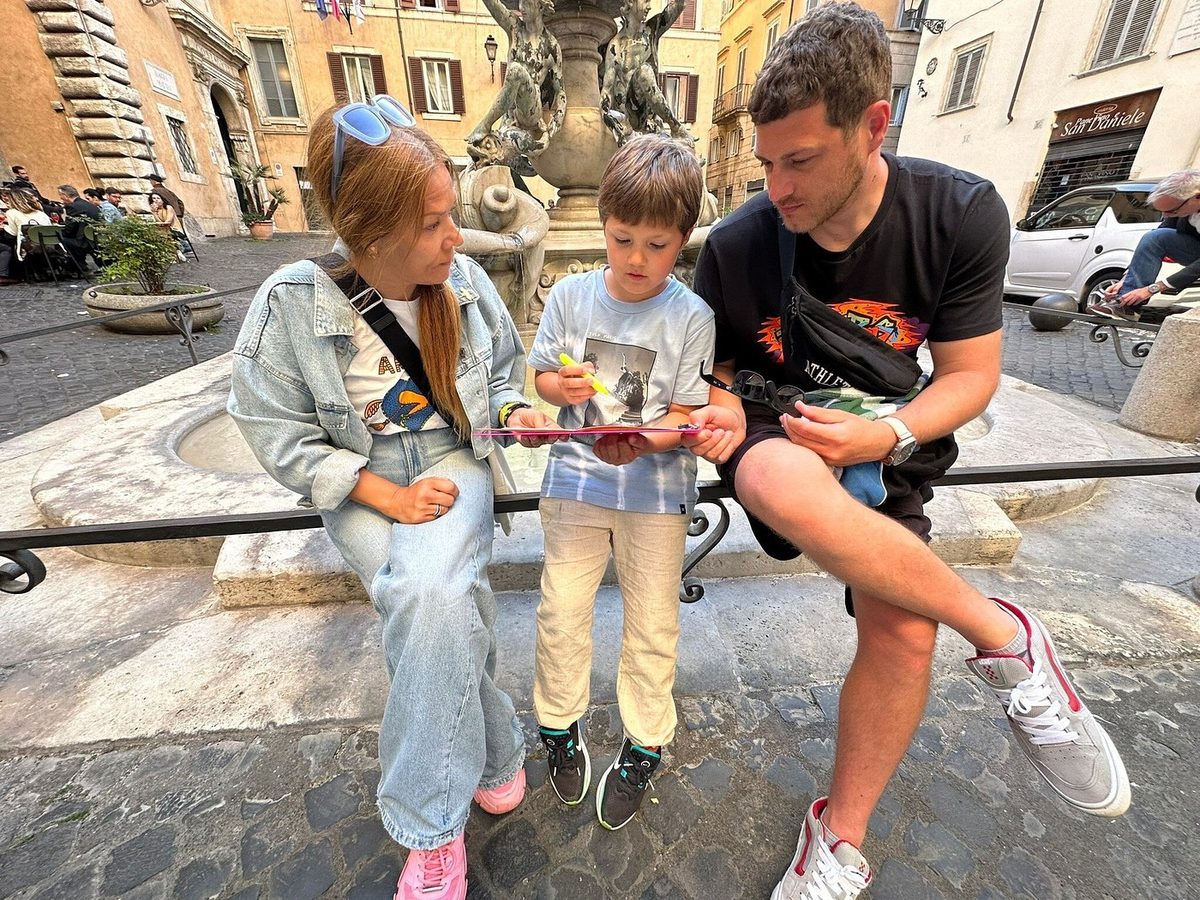 An adult and children with quest materials by a fountain