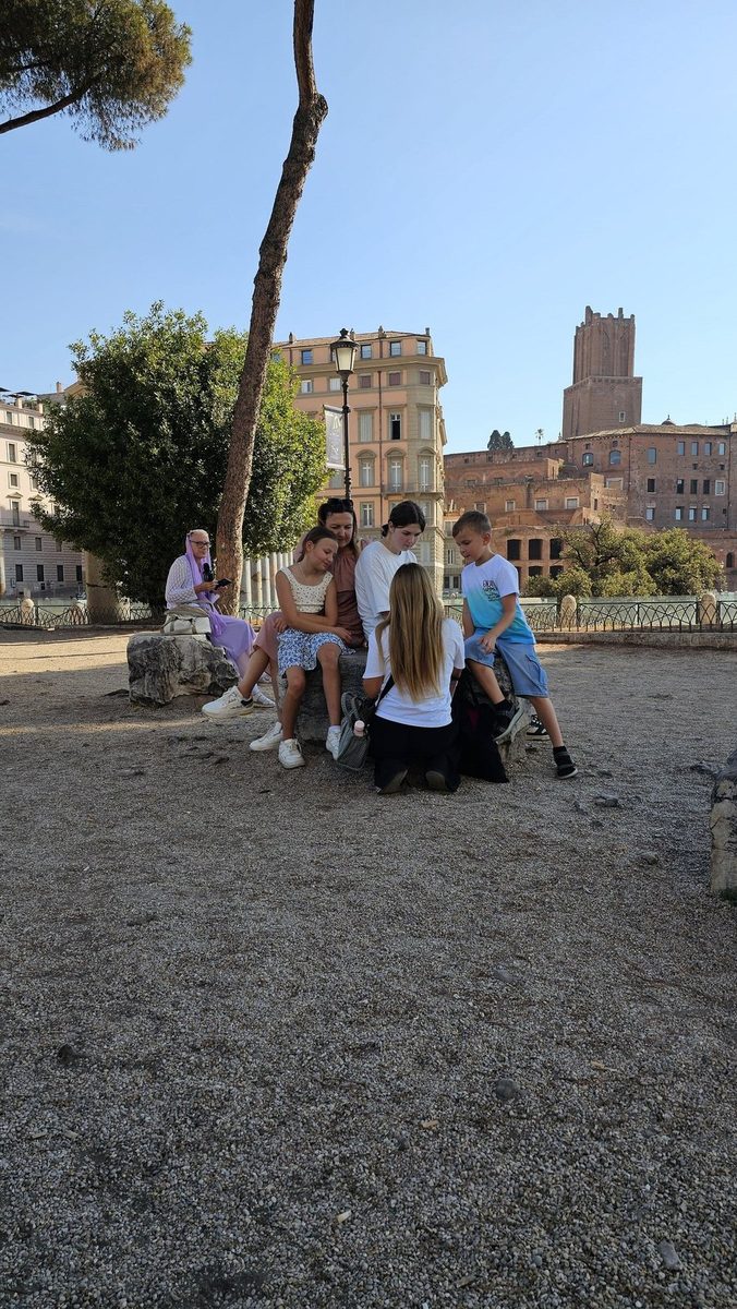 A group rests in the shade of the trees by the Forum